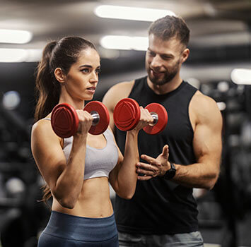 Ein Mann gibt intruktionen an eine Frau wie sie das Hanteltraining richtig ausführt.