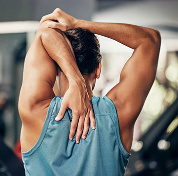 Ein mann von Hinten der mit seiner linken Hand von oben zwischen die Schulterblätter greift und mit der rechten am Ellenbogen stützt.