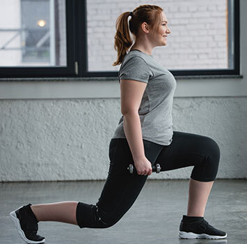 Frau im Bulgarian Split Squat mit jeweils einer Hantel in der Hand. Foto von der Seite.
